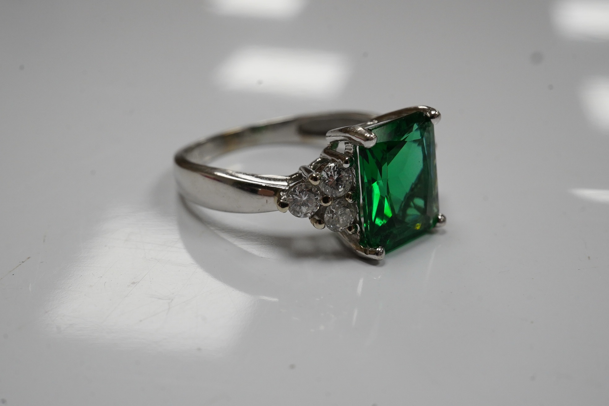 A modern 14k white metal and single stone green paste set dress ring, with six stone diamond set shoulders, size O, gross weight 3.6 grams. Condition - fair